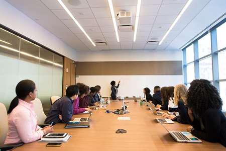 A group of people sitting at a long table watching someone give a presentation.